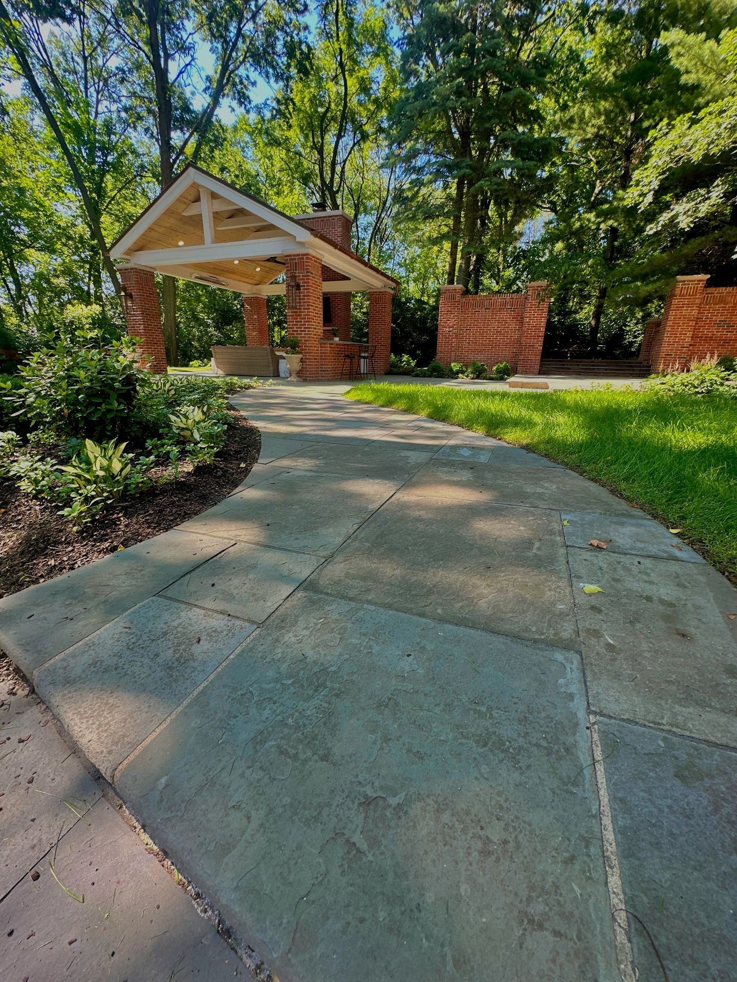 Brick and wood pavilion at end of stone path, surrounded by trees and greenery.