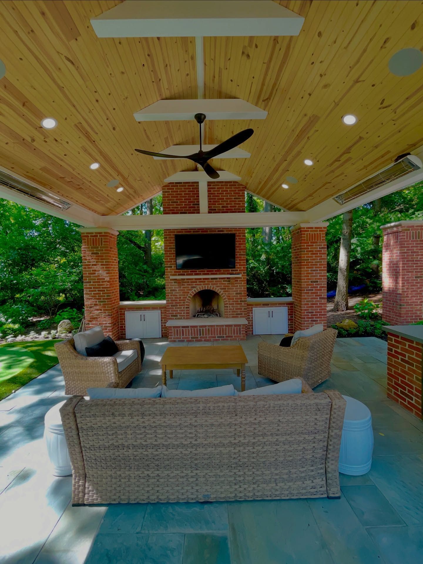Outdoor living space with wicker furniture, fireplace, TV, and wood ceiling.
