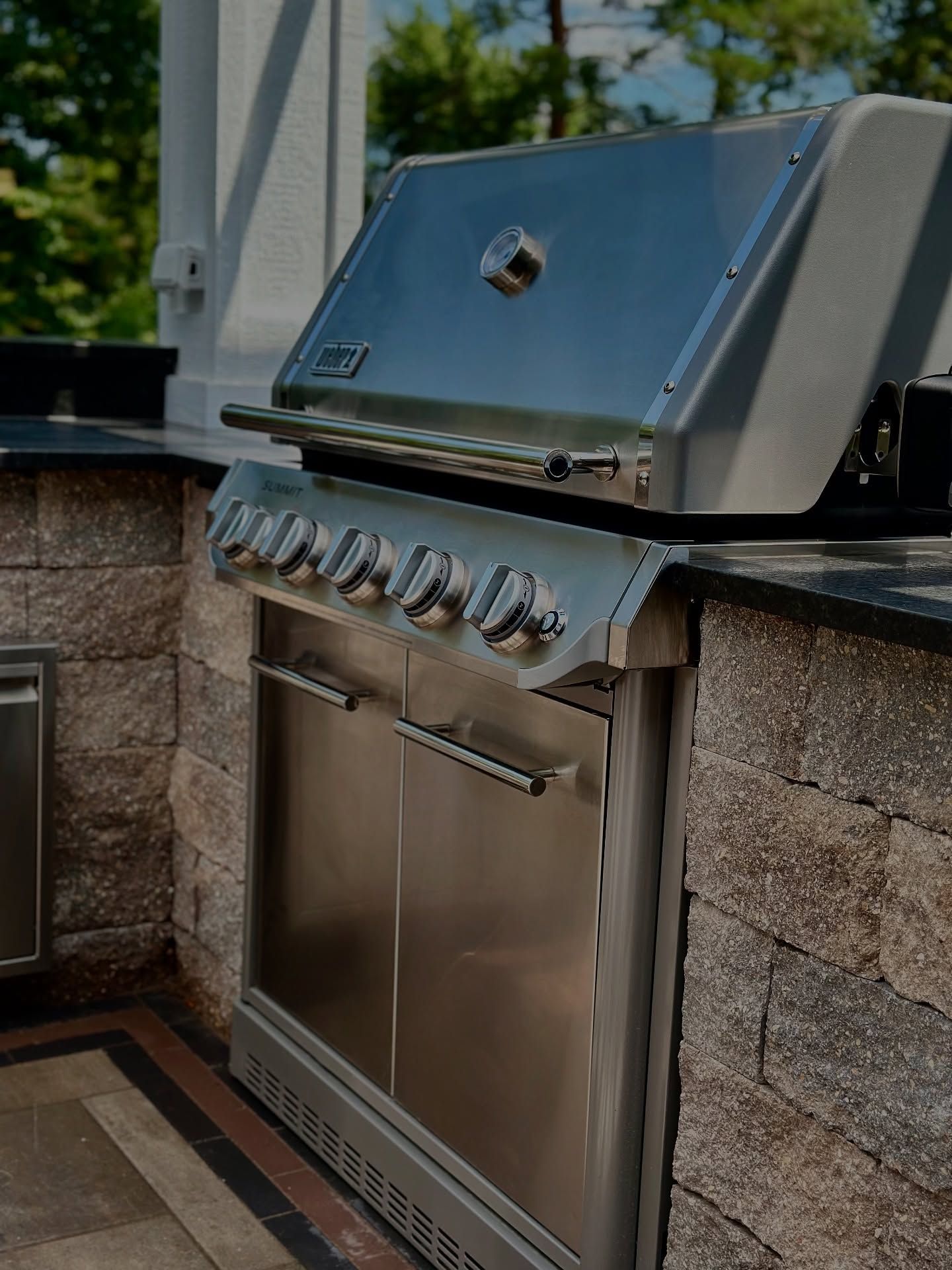 Stainless steel grill built into a stone outdoor kitchen countertop.
