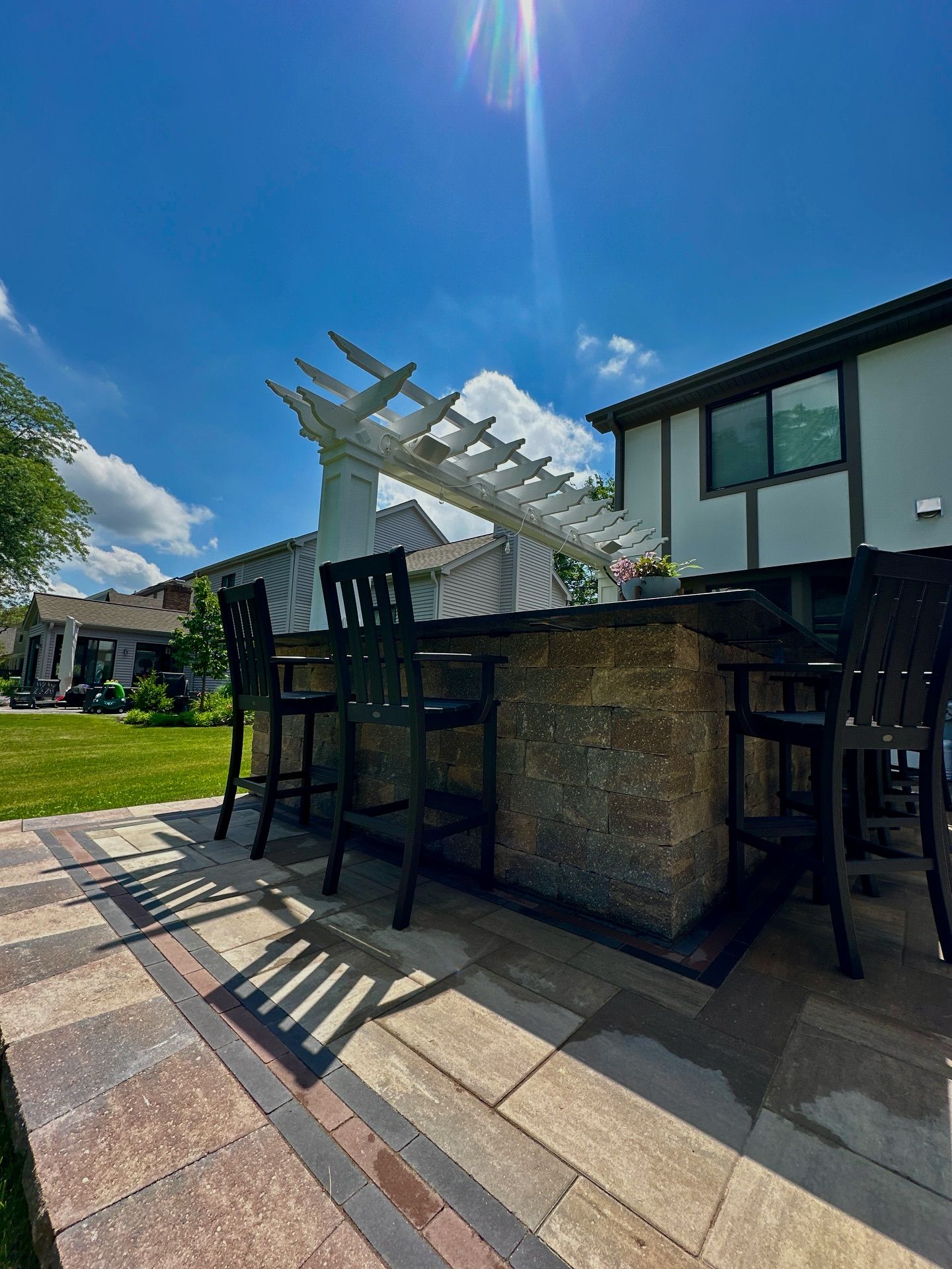 Outdoor bar with seating under a white pergola on a sunny day.