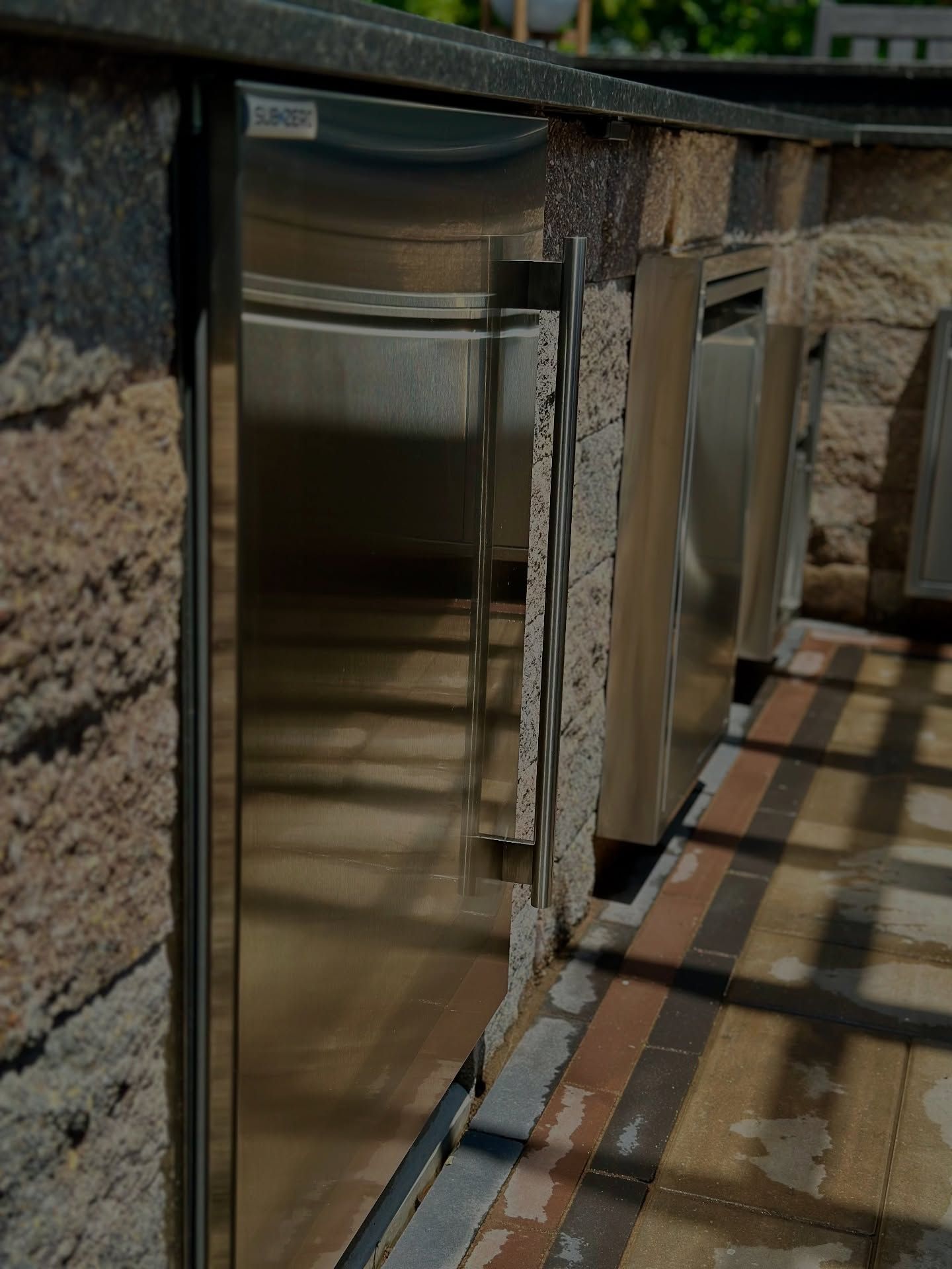 Outdoor stainless steel refrigerator built into a stone and brick counter.