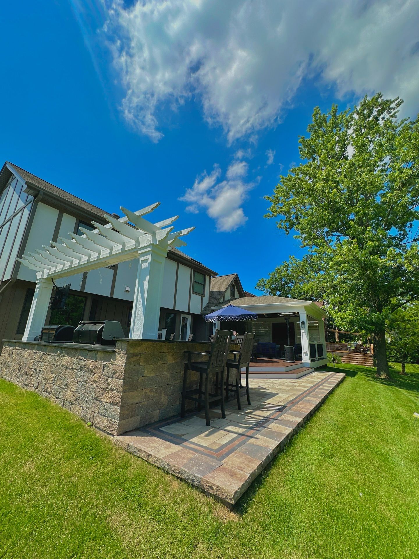 Backyard patio with bar, pergola, and house under a blue sky.
