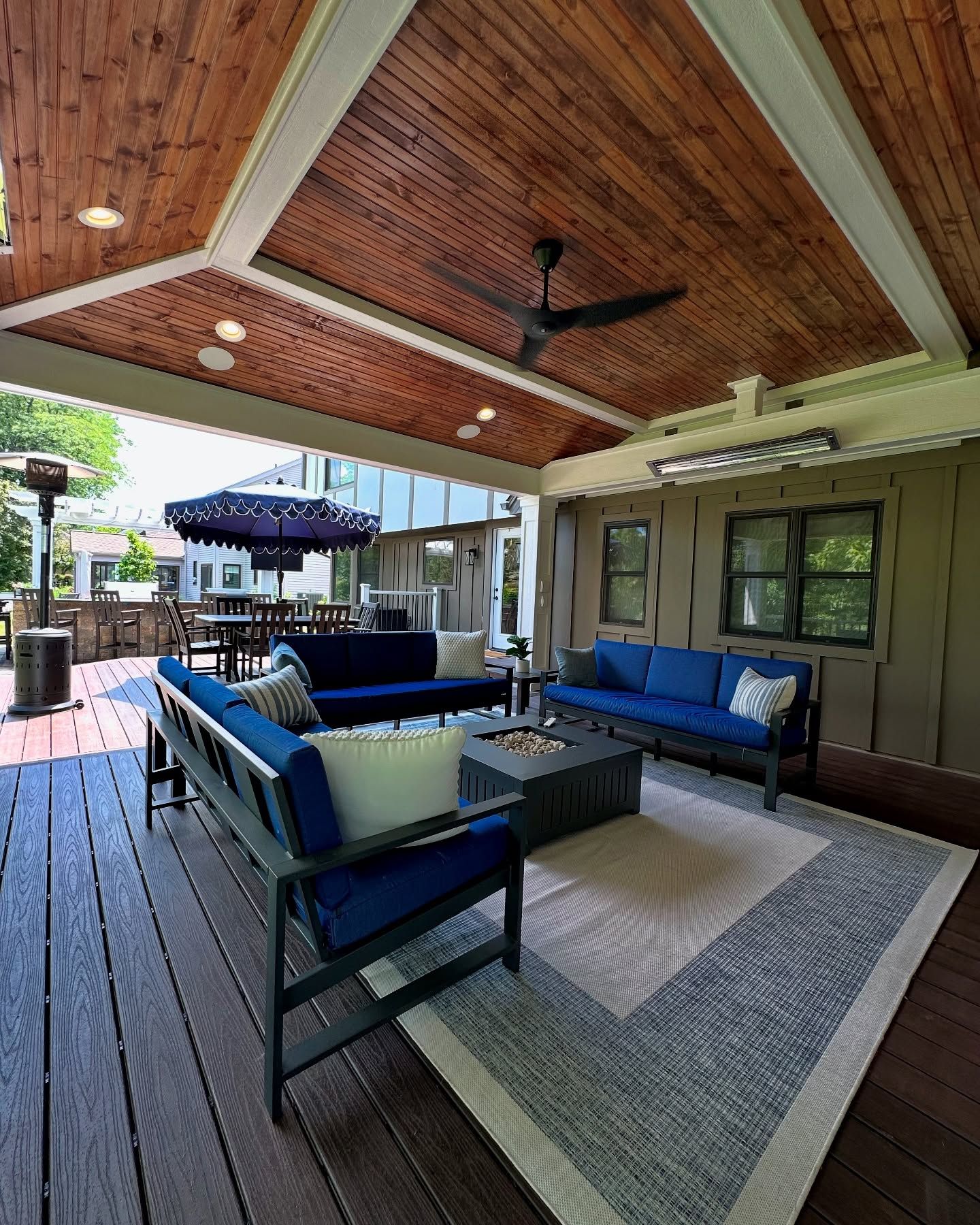 Covered outdoor seating area with wood ceiling, blue sofas, and rug.