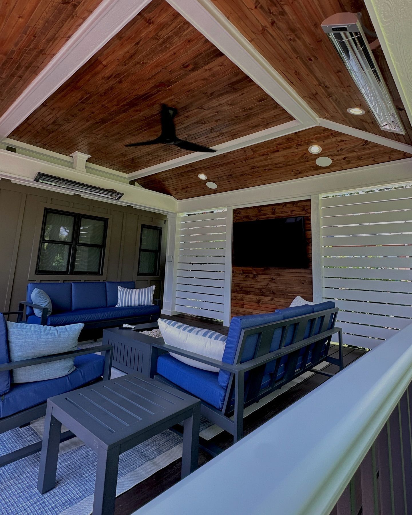 Covered patio with blue couches, wooden ceiling, and a mounted TV.