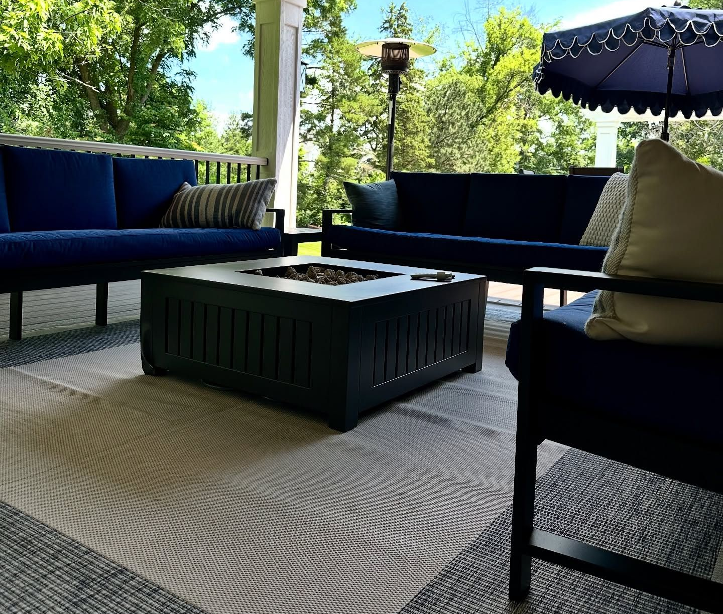 Covered patio with blue furniture, fire pit, outdoor rug, and trees in the background.