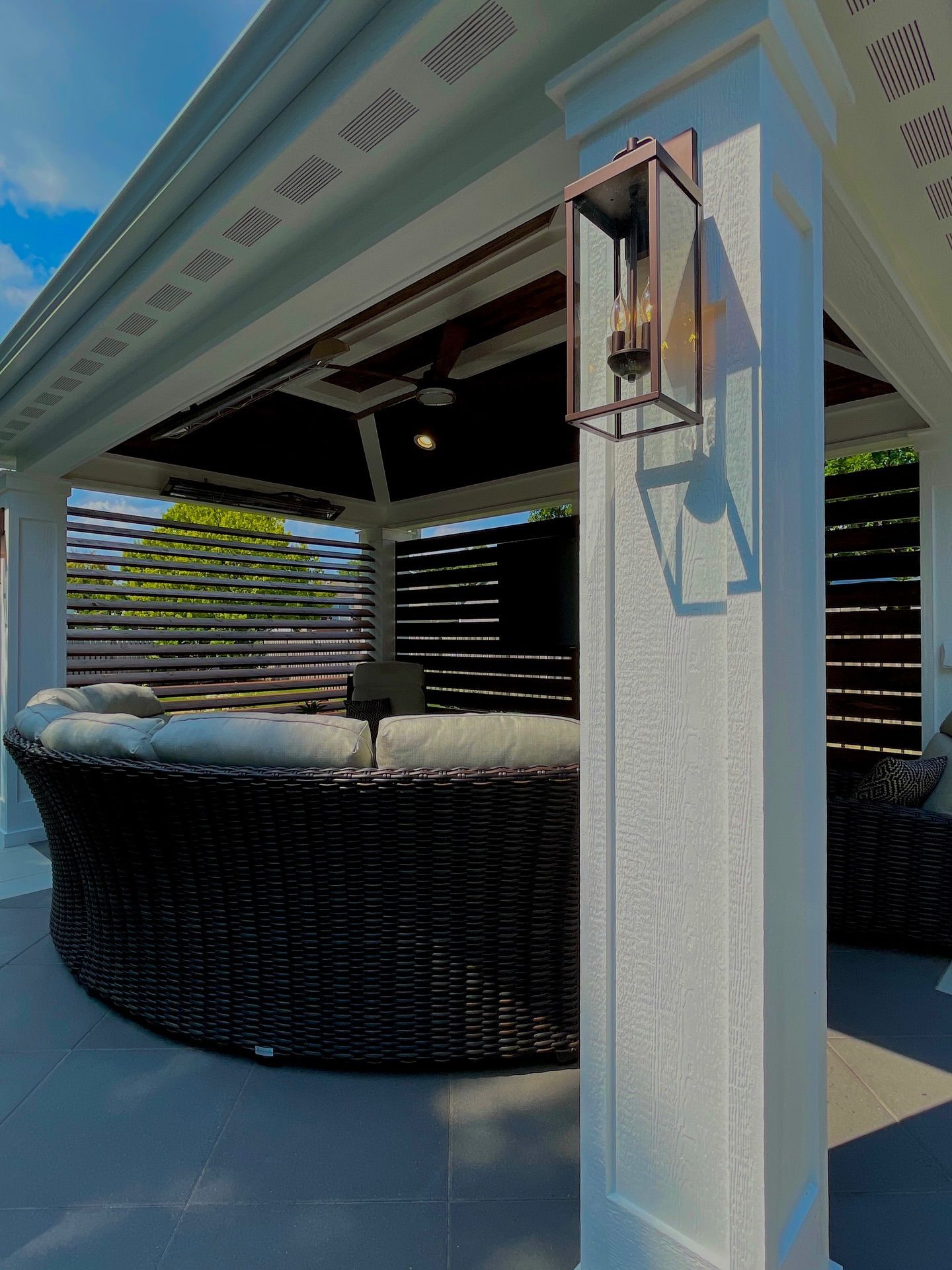 Outdoor gazebo with wicker furniture, a light fixture, and horizontal wood slats.