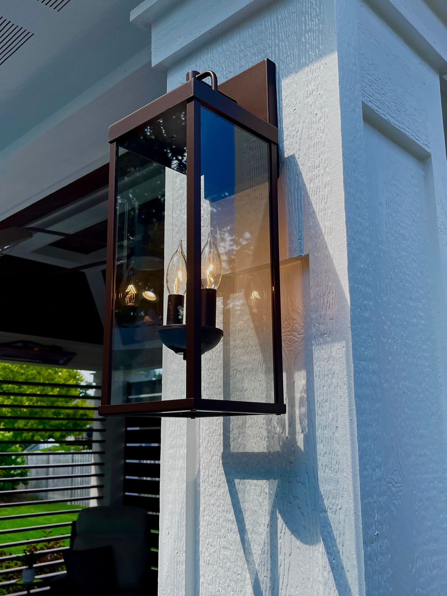 Bronze outdoor lantern with glass panels on a white textured pillar.