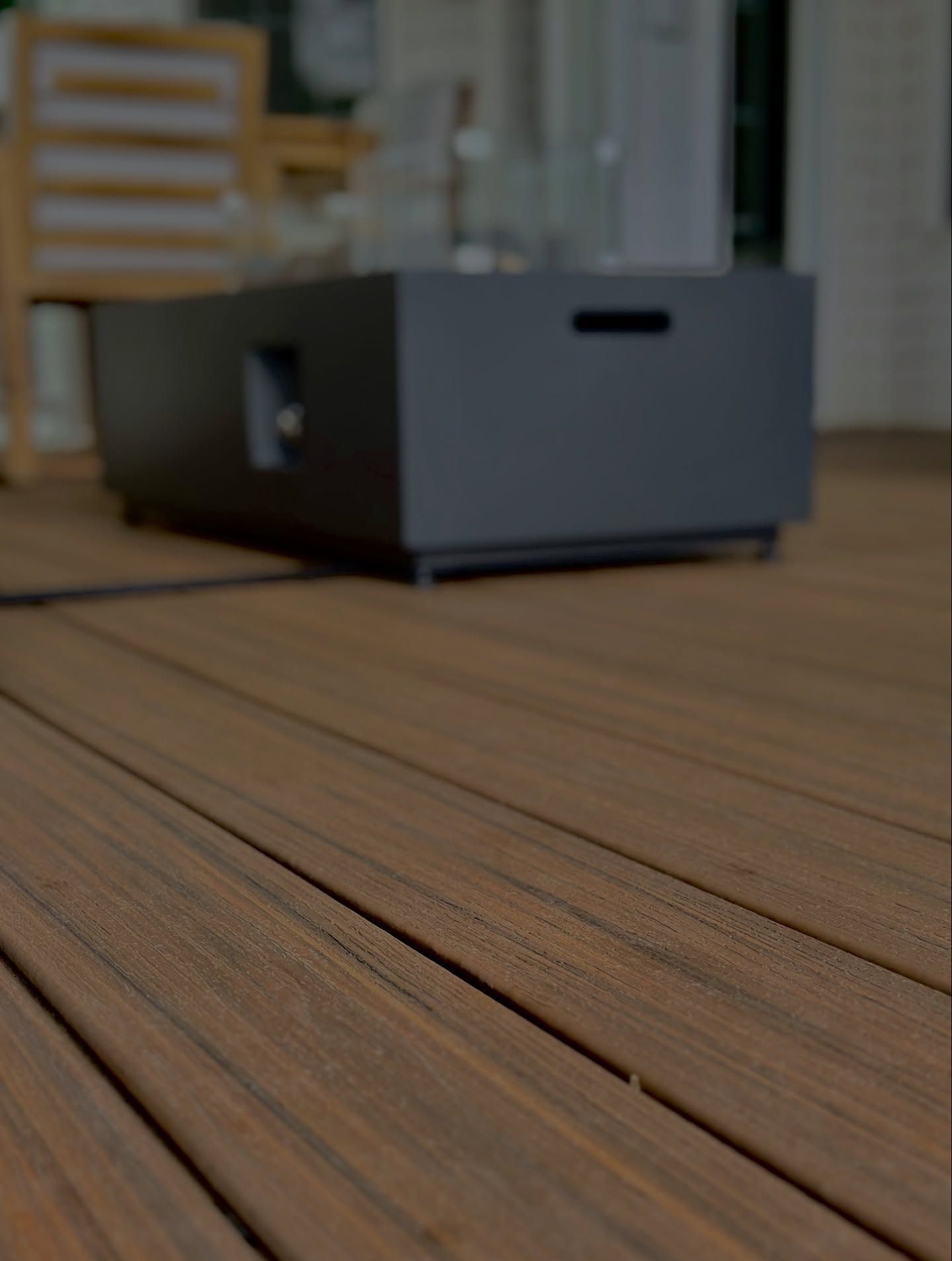 Dark brown wood deck with a gray fire pit in the background.