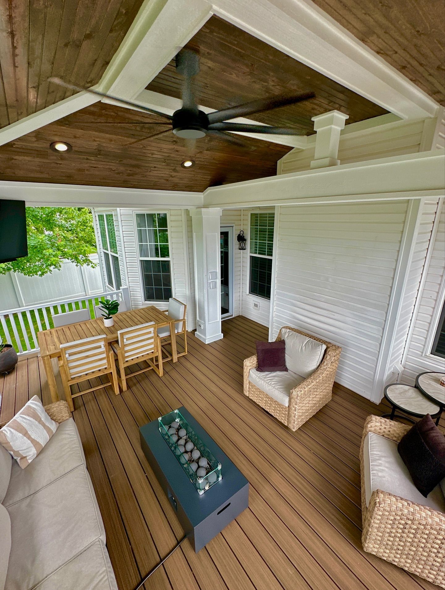 Covered outdoor living space with brown deck, wooden ceiling, and seating.