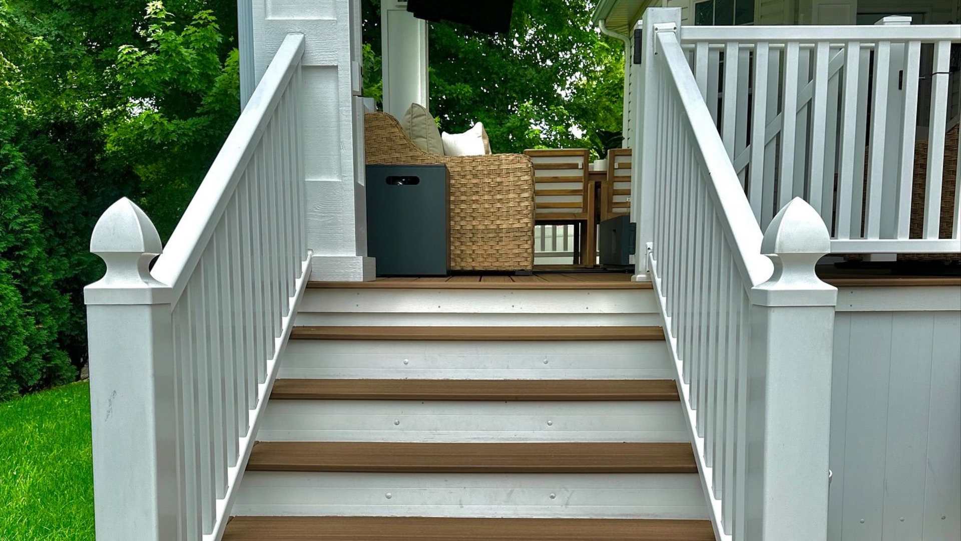 White painted staircase leading up to a porch with a grill, wicker basket, and chairs.