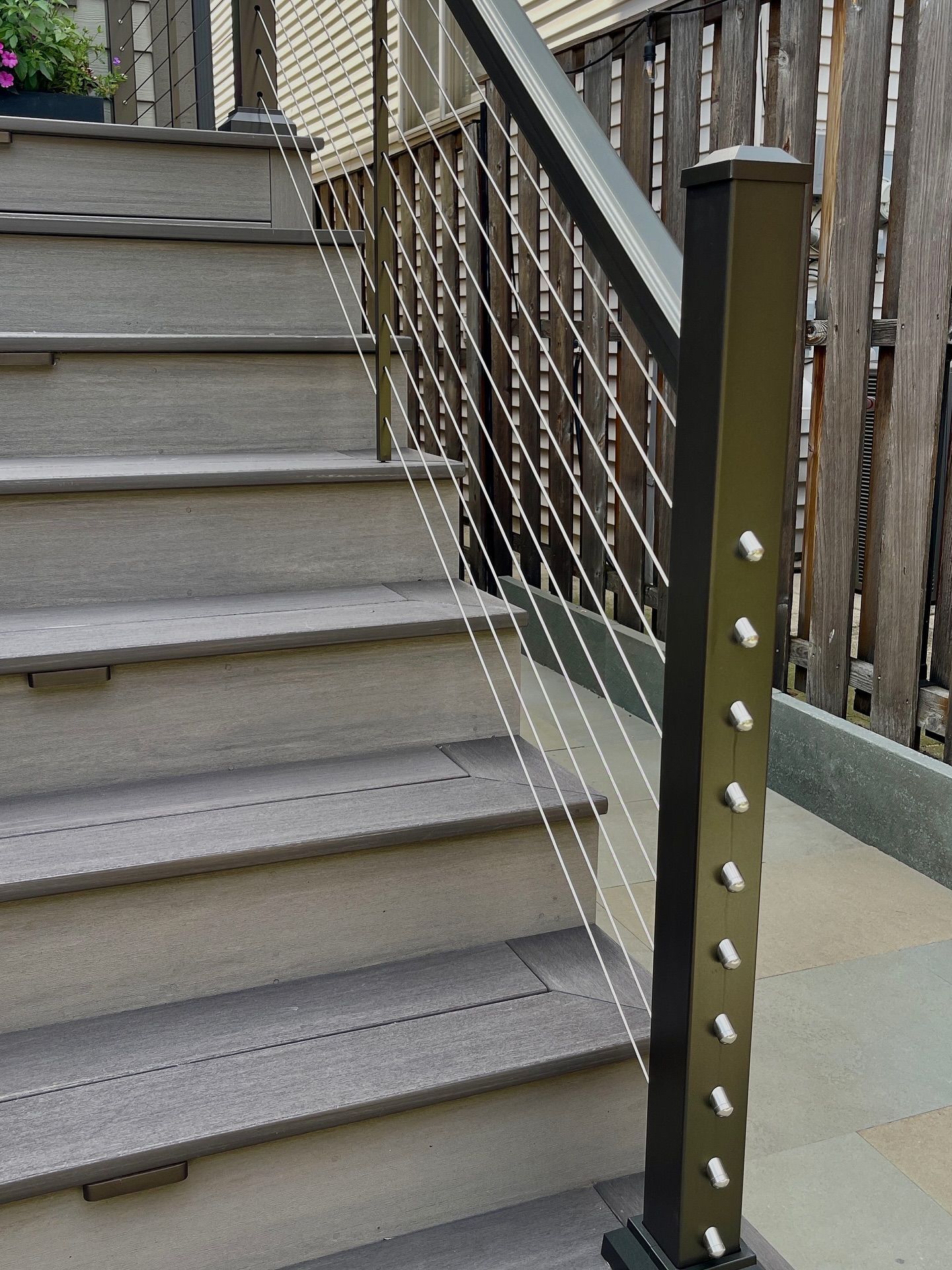 Staircase with gray composite steps and a black metal railing with cable infill.