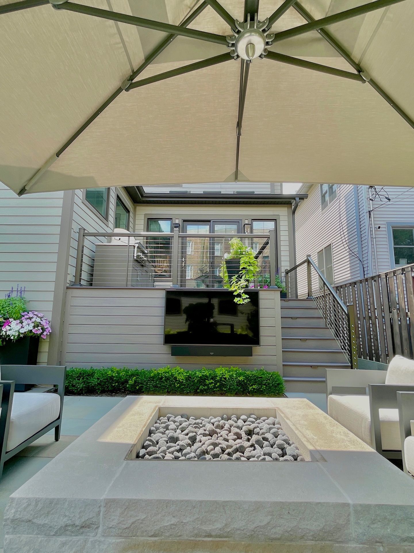 Outdoor patio with fire pit, TV on wall, umbrella, and seating. Gray tones.