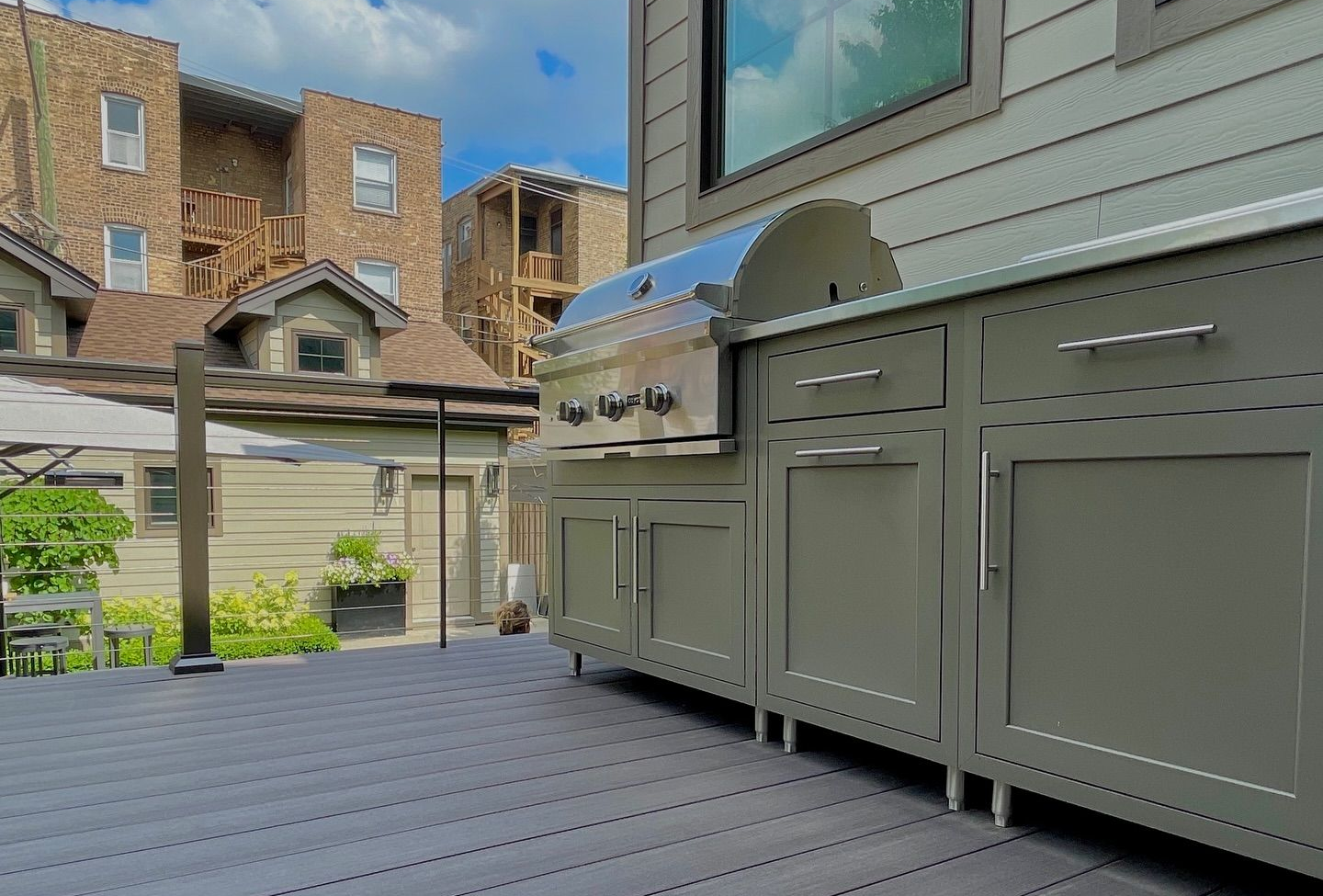 Gray composite deck with outdoor kitchen and stainless steel grill under a sunny sky.