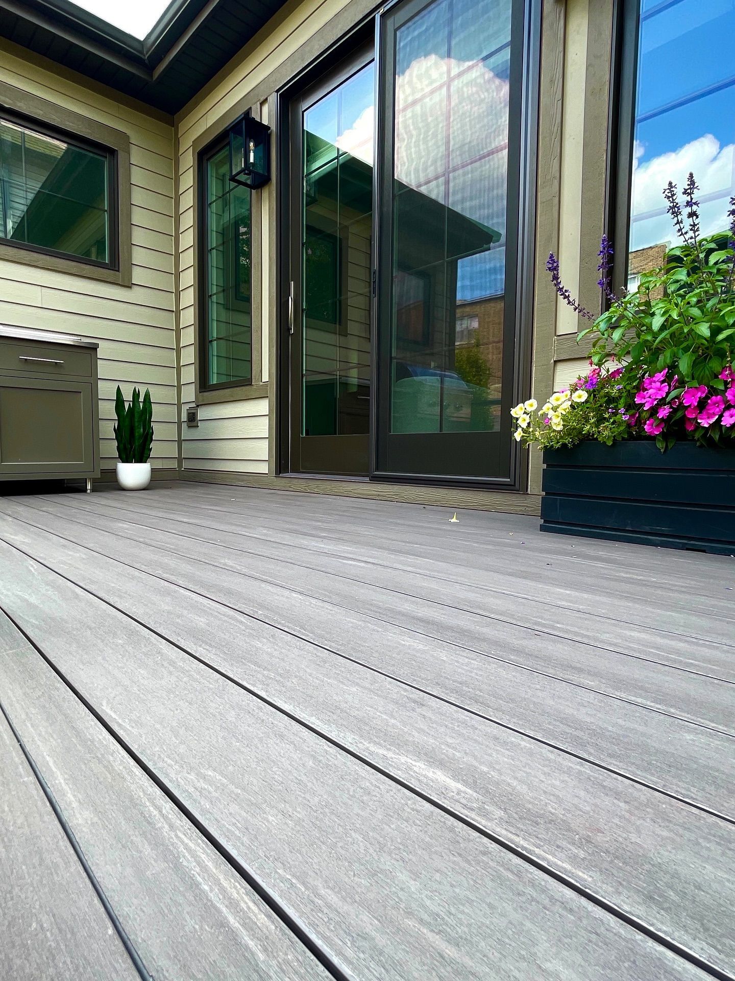 Composite deck with sliding glass doors, flower box, and beige siding.