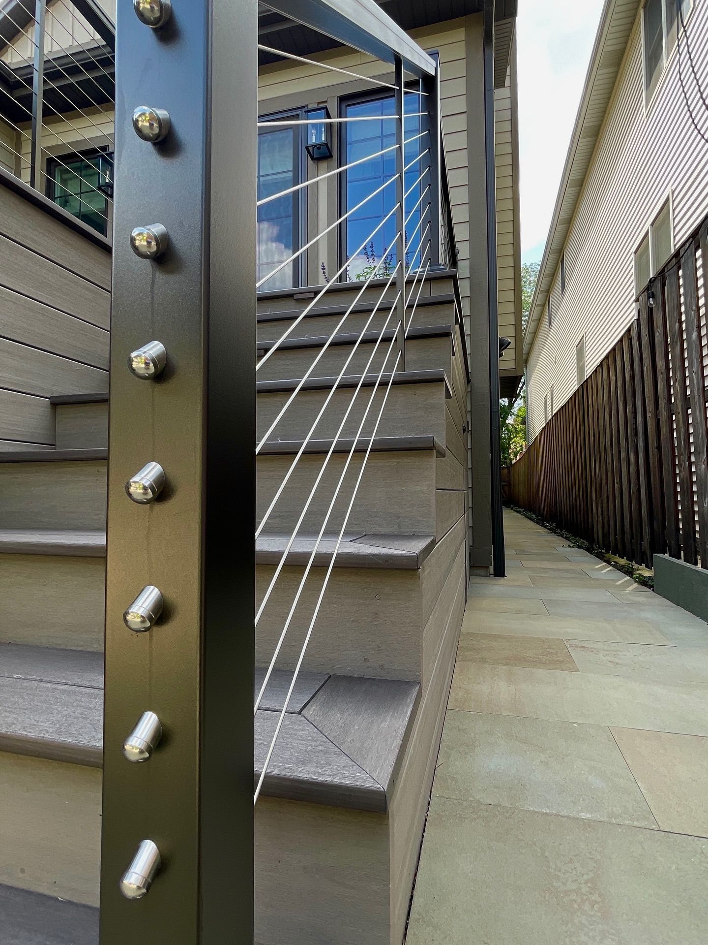 Modern staircase with gray steps and black metal post with stainless steel cable railing. Exterior setting.