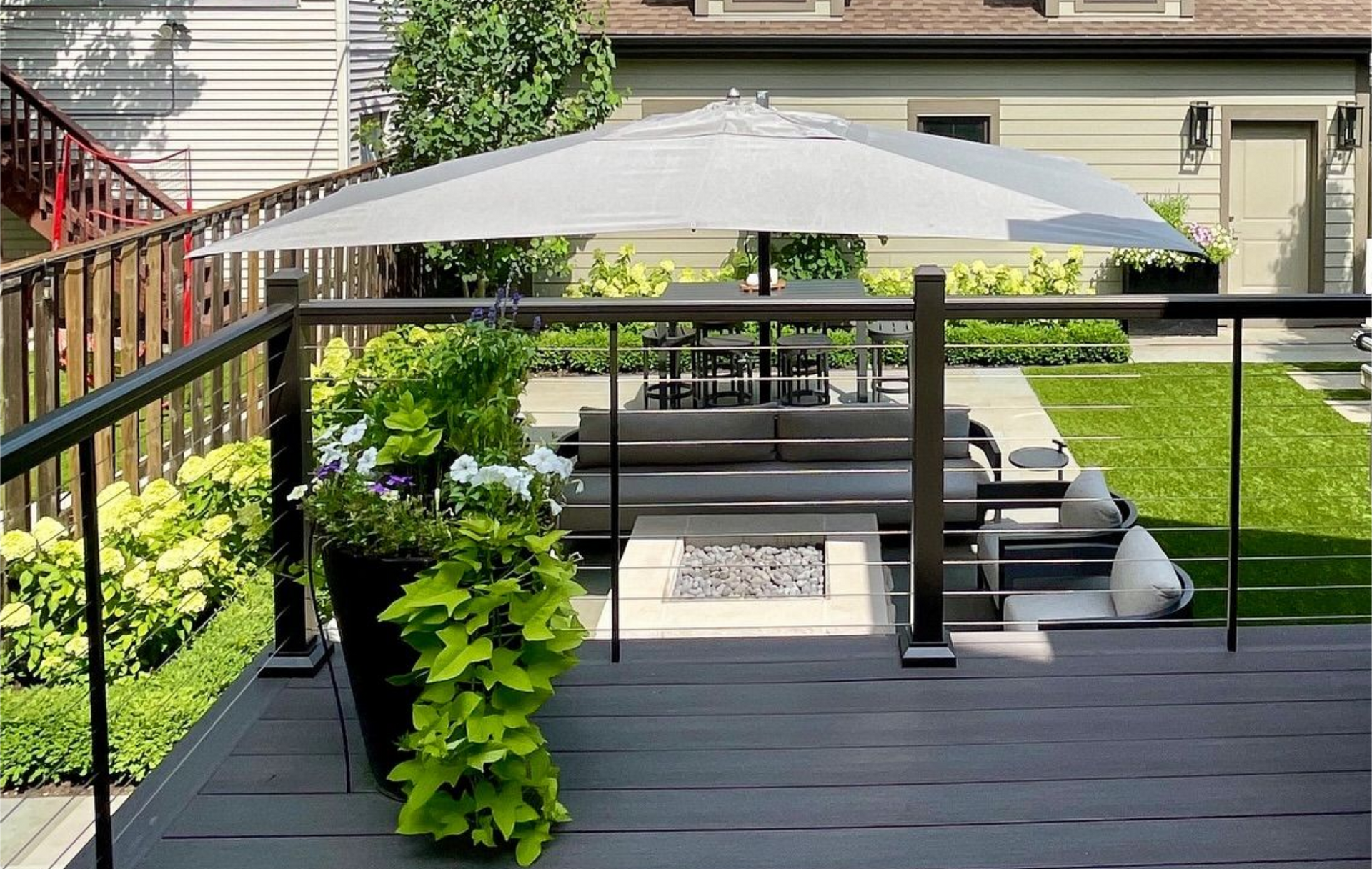 Backyard patio with umbrella, seating area, lawn, and multi-story brick building in background.