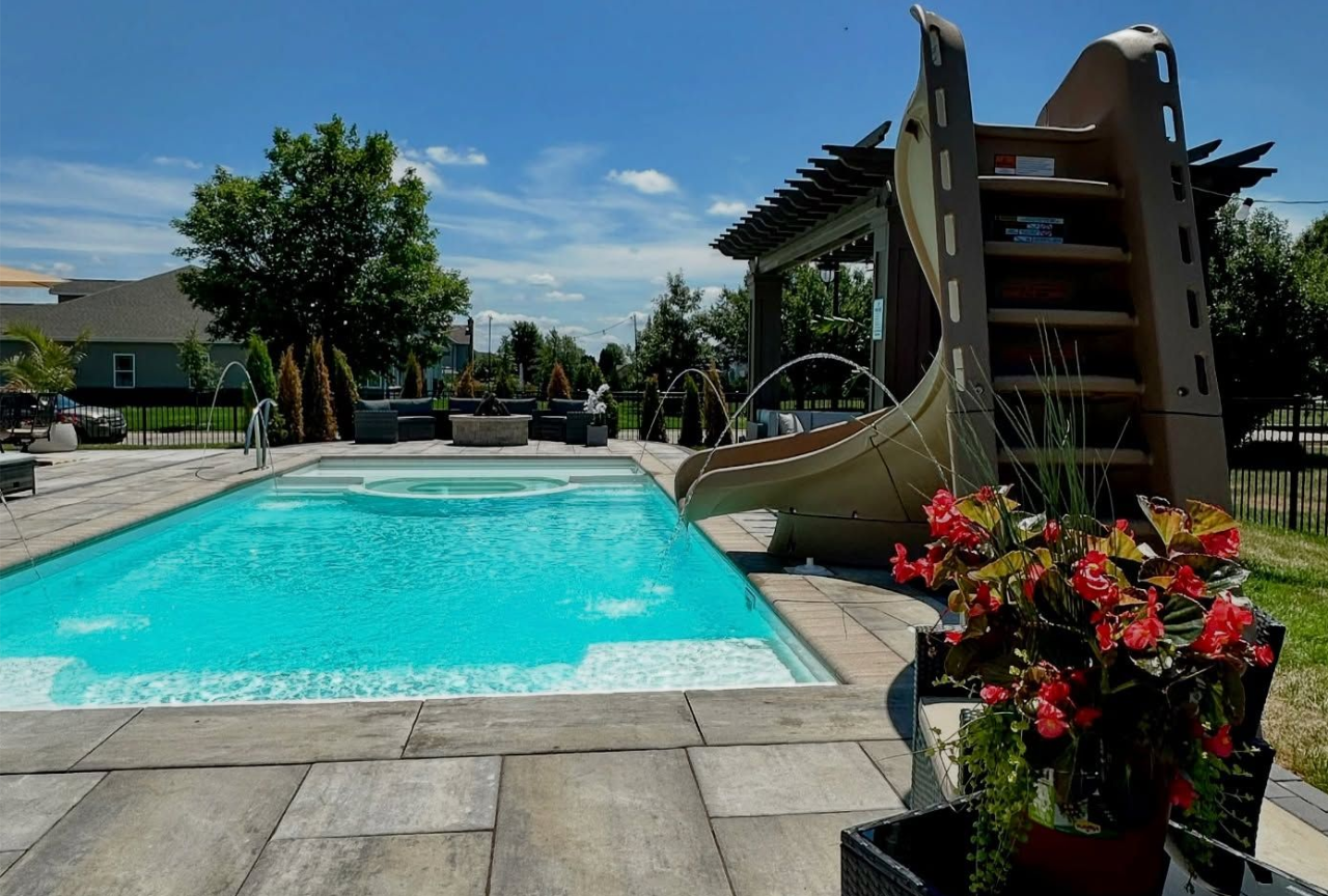 Swimming pool with slide, patio furniture, and flowers on a sunny day.