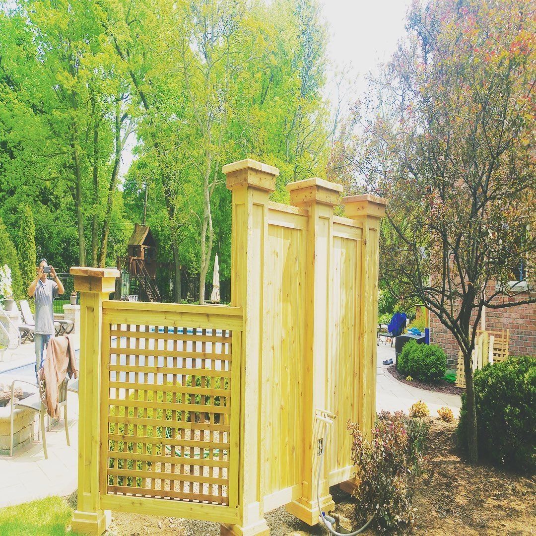 Wooden privacy fence with lattice panel and ornate posts, near trees and a pool.