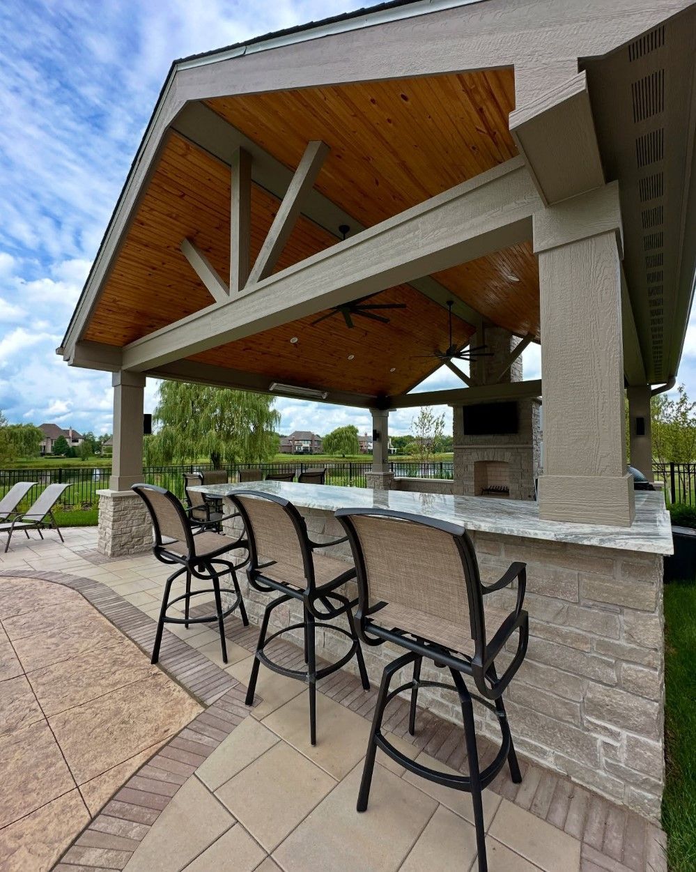 Outdoor covered bar area with seating, countertop, and fireplace; wood ceiling.