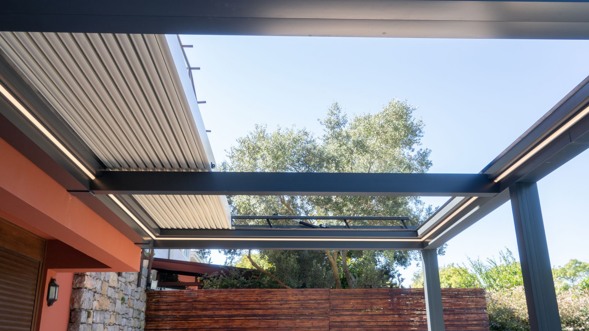 Pergola with adjustable roof slats and built-in LED lighting, viewed from below, against a blue sky.