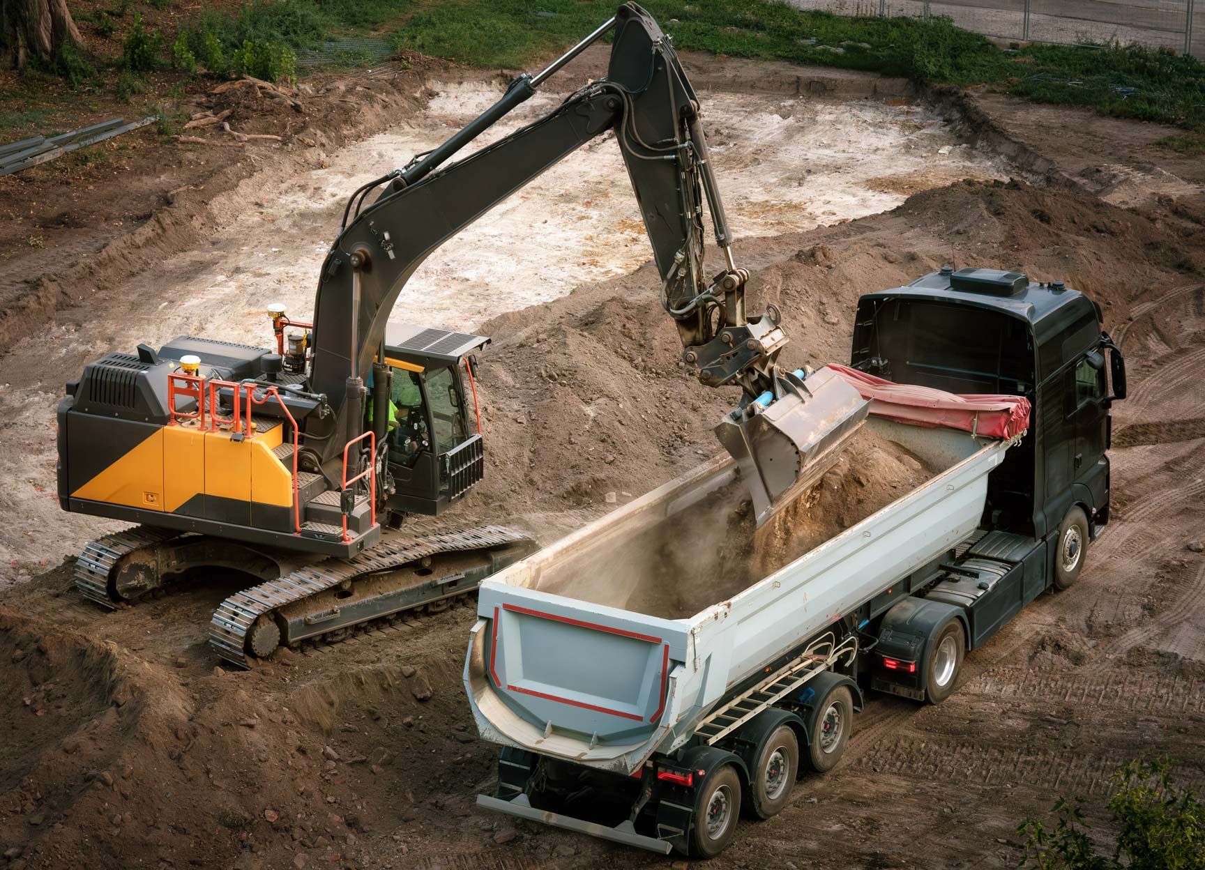 Excavator loading dirt into a dump truck at a construction site.