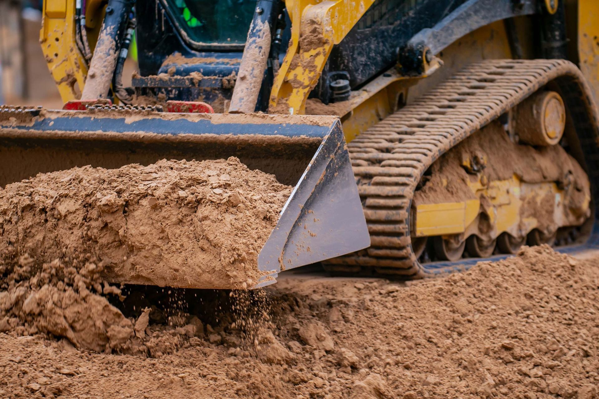 Yellow skid steer digging into brown dirt.