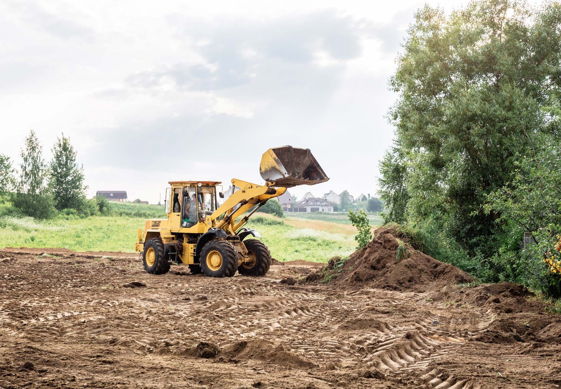 Yellow loader moving dirt in a field on a cloudy day.