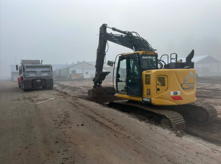 Yellow excavator digging dirt at a construction site, crane in the background.