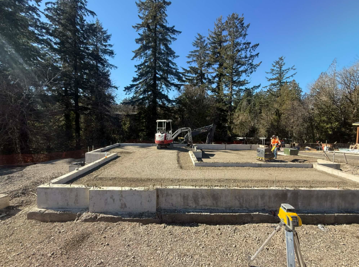 Yellow excavator on a construction site digging dirt under a bright blue sky.