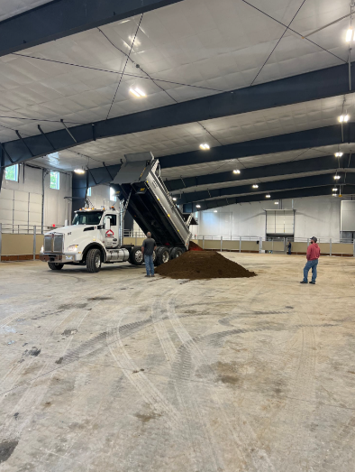 Yellow excavator loading a red dump truck with dirt in a wooded area.