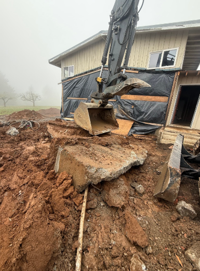 Yellow excavator demolishing a building, with dust rising against a blue sky.