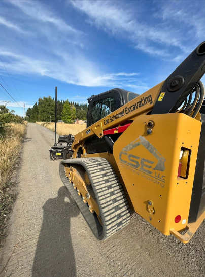 Yellow excavator digging in a dirt pile, with a colorful sky in the background.