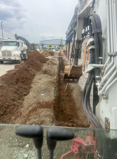 Underground trench with black corrugated pipe and multiple black cables laid in sand.