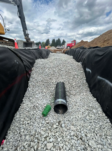 Yellow excavator digging in a deep trench under a cloudy sky.