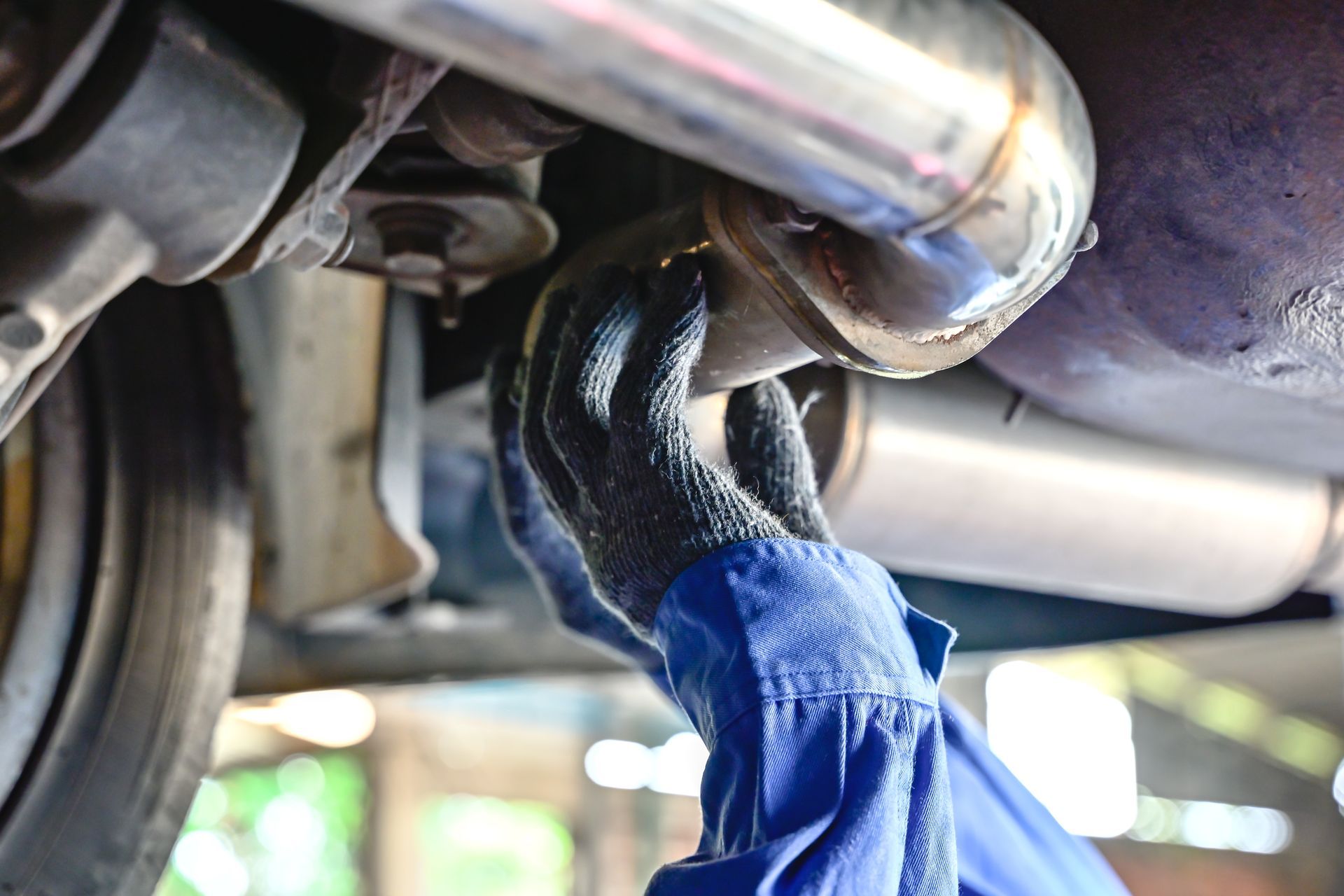 Mechanic’s gloved hands inspecting a car’s exhaust pipe under the vehicle. Mechanic’s gloved hands inspecting a car’s exhaust pipe under the vehicle.