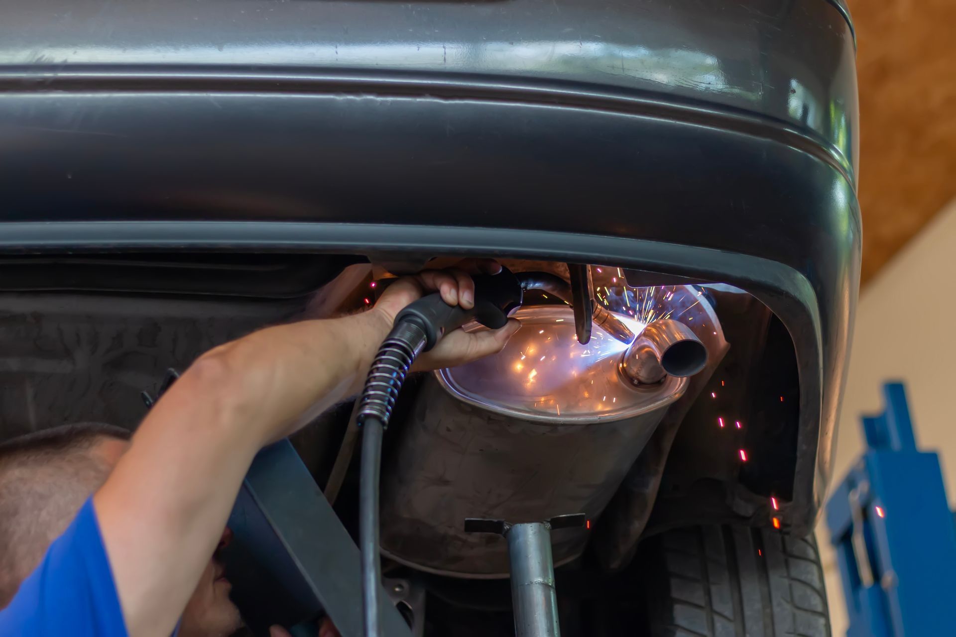 A mechanic at a muffler repair shop is replacing the rear muffler of the exhaust system in a car.