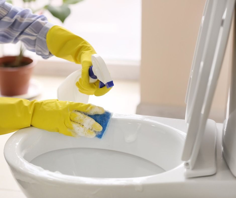 Une personne portant des gants jaunes nettoie les toilettes avec une éponge.