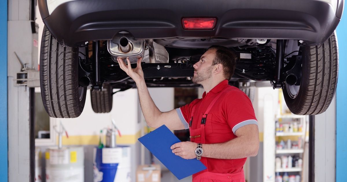 A vehicle is lifted up, and a man in a red shirt is inspecting the muffler.
