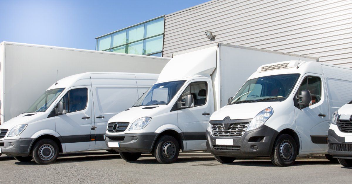 A group of white fleet vans parked in front of a warehouse building.