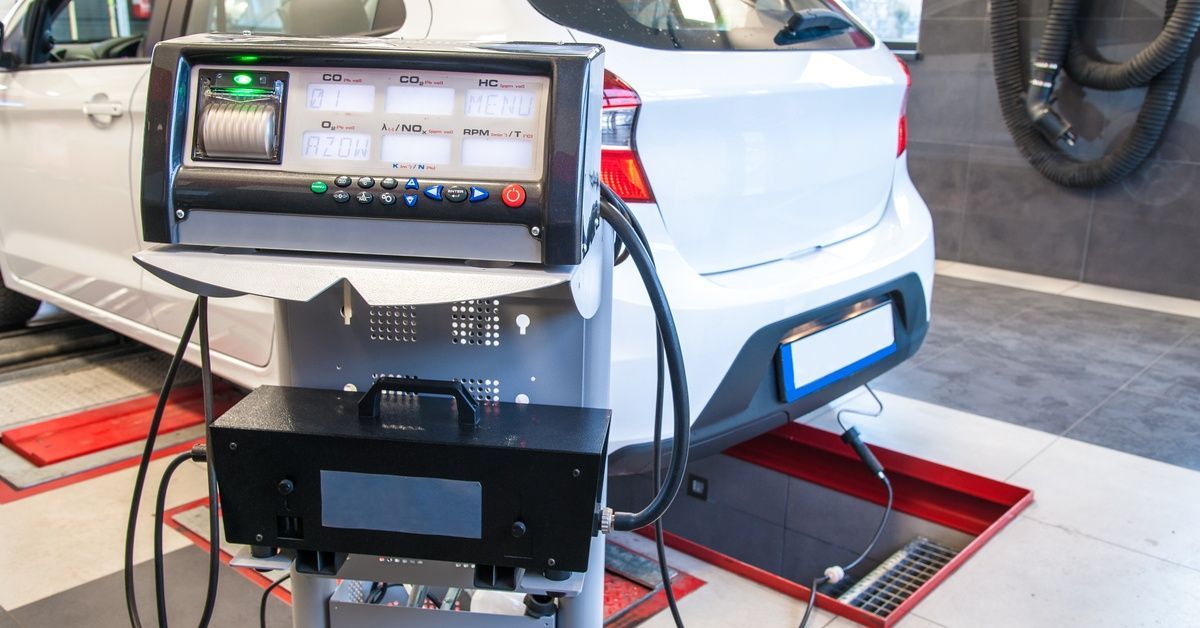 A white hatchback car is being tested at a diagnostic station. Connected to it is a diagnostic tool.