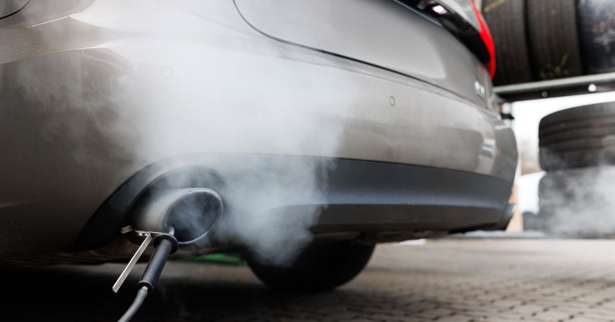 A vehicle at a diagnostic center emits dense smoke from its exhaust pipe, to which with an emission scanner is attached.