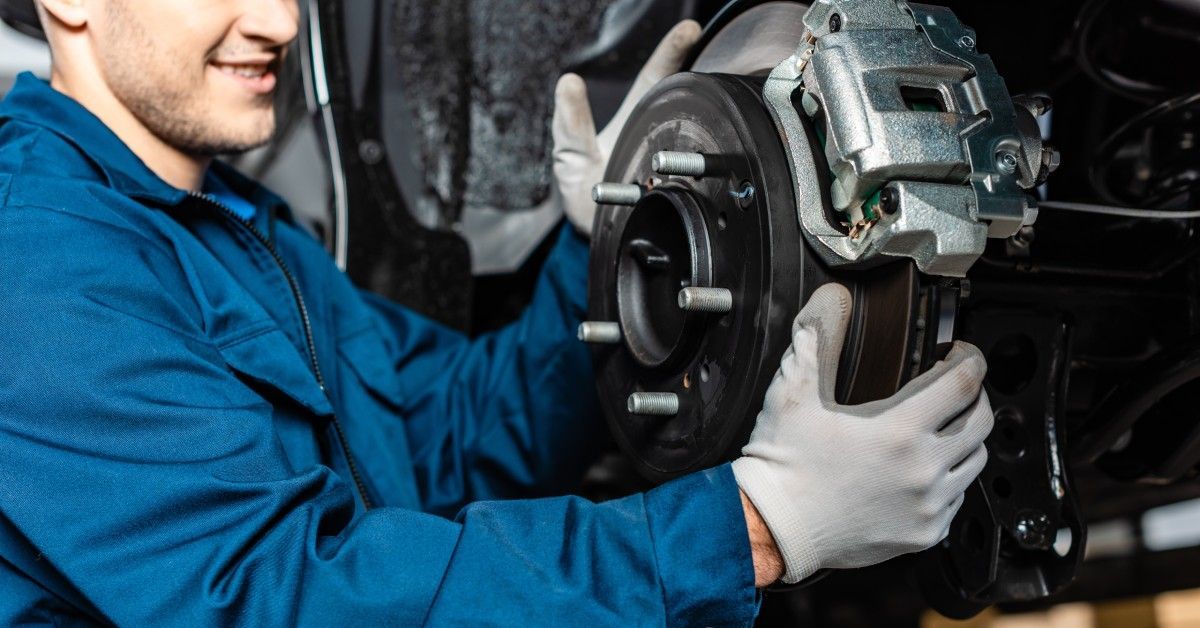 A mechanic wearing gloves smiles while adjusting the disk brakes of a car.