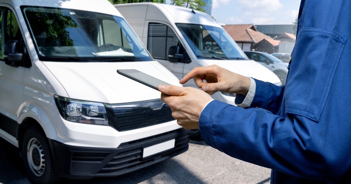 A man in a blue uniform holds a tablet while standing next to a fleet of vans.
