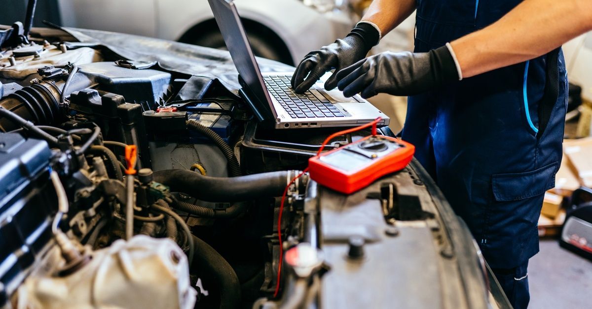 A car mechanic uses a laptop and digital multimeter to diagnose a vehicle.
