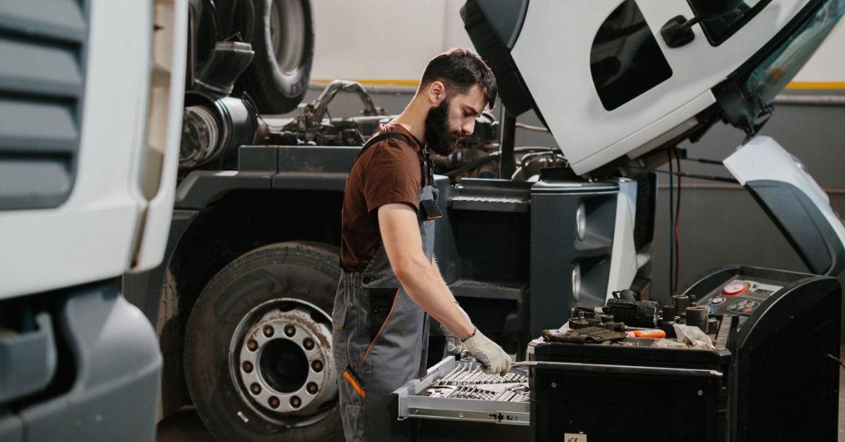 A mechanic wearing a brown shirt is sorting through tools for repairing a truck.