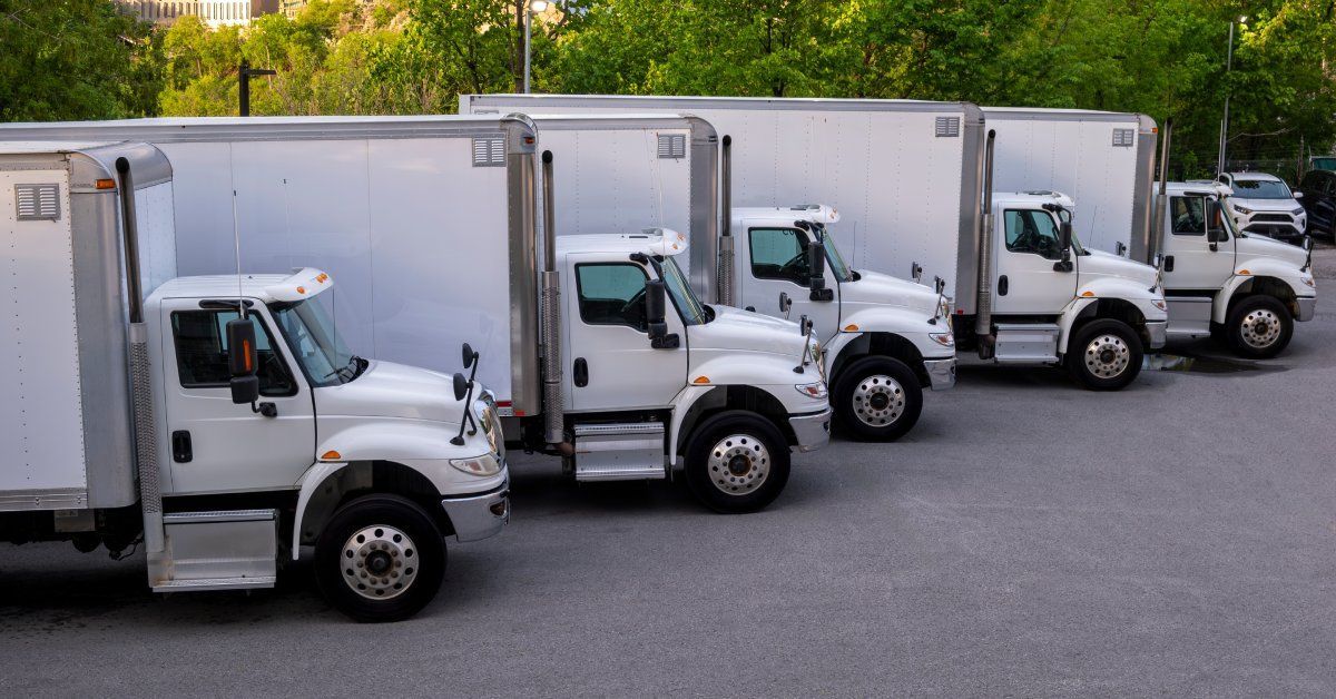 A fleet of white refrigerated trucks sit in a row while parked on the pavement.