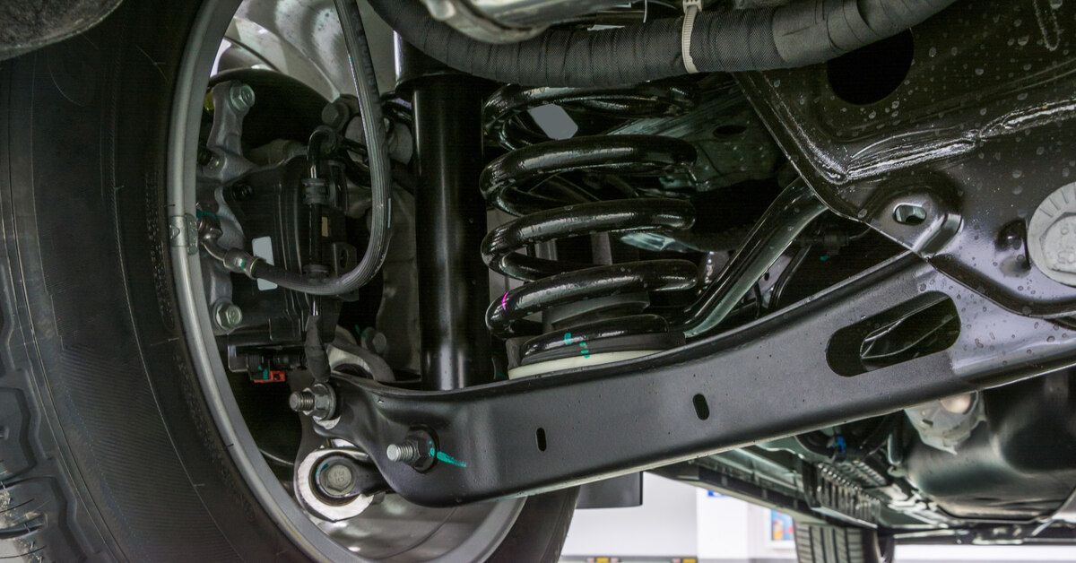 Close-up of a rear suspension on a car, connected to a wheel. A giant metal spring is visible under 