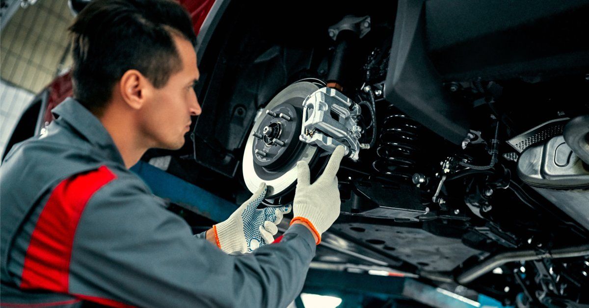 A mechanic wearing white gloves adjusts the suspension of a lifted red car.