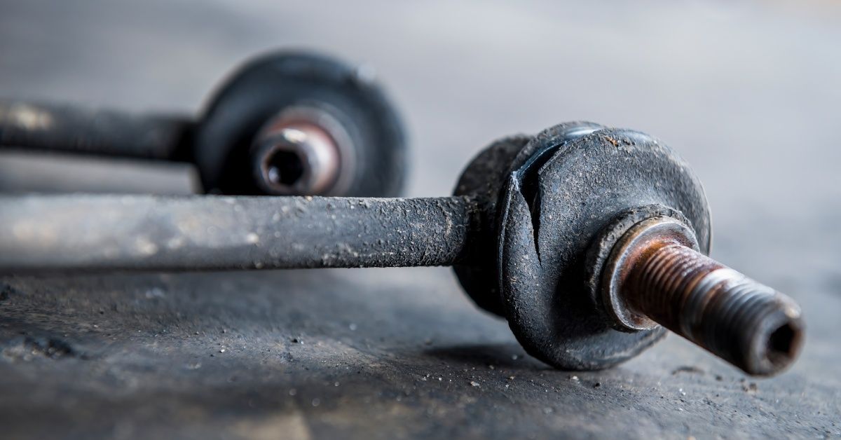 A rusty and broken stabilizer sway bar link laying on the ground.