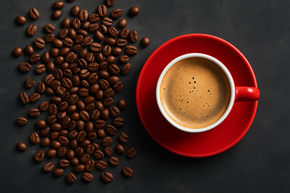 A cup of coffee on a red saucer next to a pile of coffee beans.